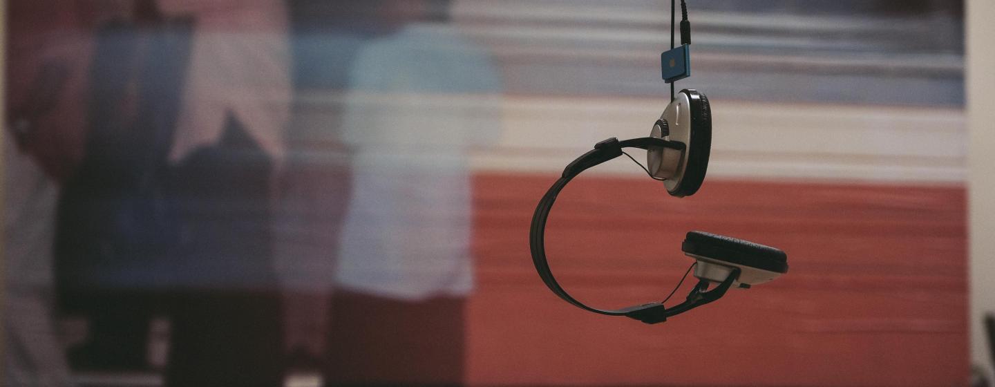 Headphones hanging from a cord in front of a blurred poster 