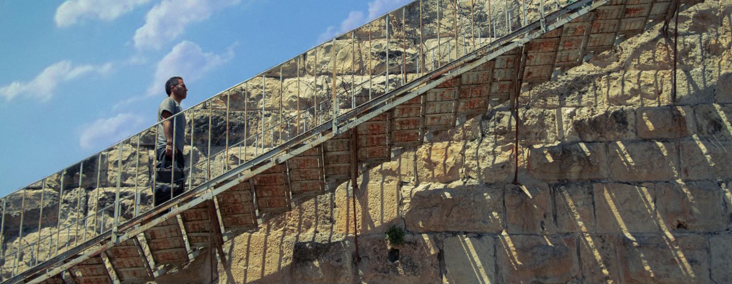 An image of a man walking up a set of stairs with a wall and the blue sky behind him 