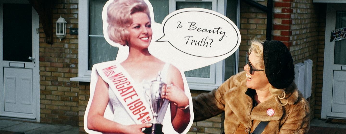 A cardboard cut out of a beauty queen with a smiling woman in sunglasses and a hat