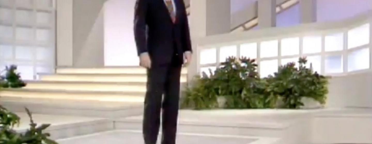 An image of a man in a suit, on a talk show set