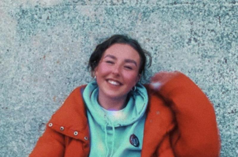 A person in a red jacket, smiling in front of a wall