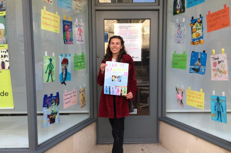 A young woman holding a poster standing outside a window