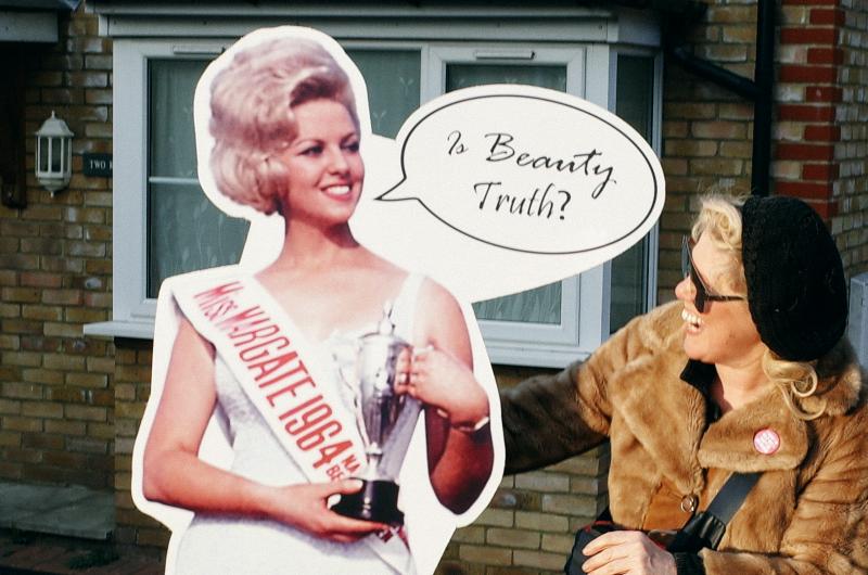 A cardboard cut out of a beauty queen with a smiling woman in sunglasses and a hat