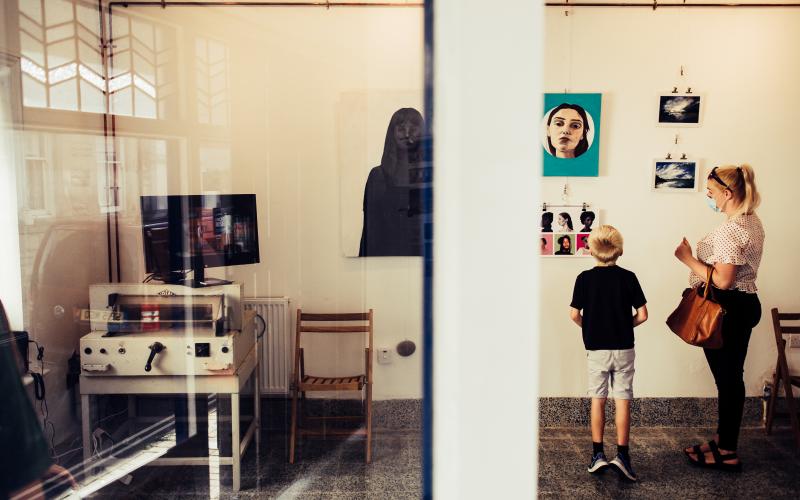A mother and child in an exhibition room, looking at artwork on the walls