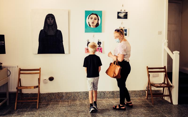 A mother and child in an exhibition room, looking at artwork on the walls