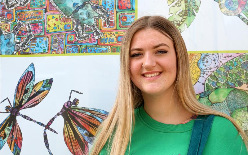 A smiling young woman standing in front of highly coloured drawings